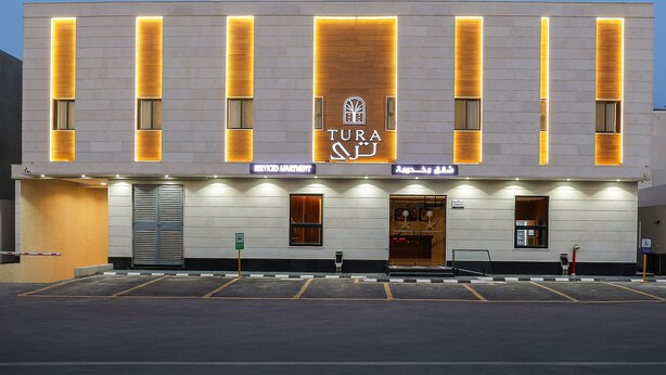 A modern hotel with a service entrance, parking, and illuminated signage. - Tura Residence Al Khaleej (Riyadh)