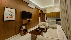 A modern living room with a flat-screen TV, a coffee table, and a sofa. There is a framed artwork on the wall and a wooden cabinet below the TV. - Tura Residence Al Khaleej (Riyadh)