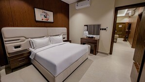 A hotel room with a large bed, a wooden headboard, a desk with a mirror, and a wall-mounted air conditioner. - Tura Residence Al Khaleej (Riyadh)