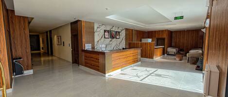 A spacious lobby with a reception desk, seating area, and a marble wall.