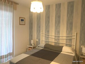 Ein Schlafzimmer mit Bett, Nachttisch, Lampe, Vorhang und einer Wand mit vertikalen Streifen.