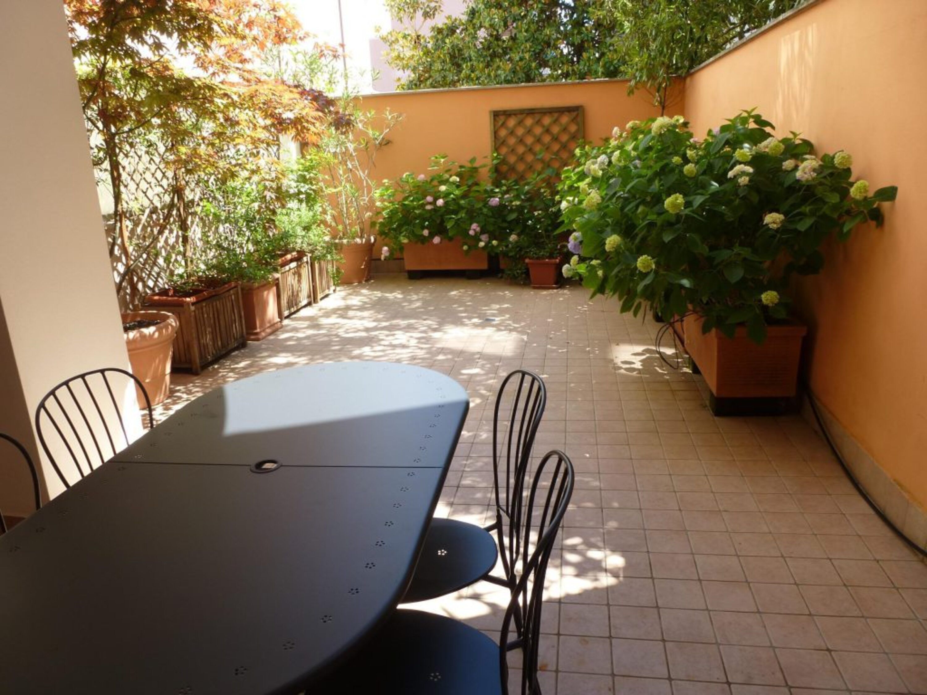 Een terras met een tafel en stoelen, omgeven door potplanten en een betegelde vloer.