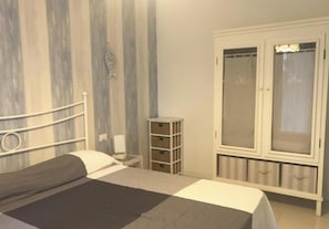 A bedroom with a bed, a wardrobe, a bedside table, and a wall with vertical stripes. - Lovely Private Garden Apartment for Four in Grado (Grado)