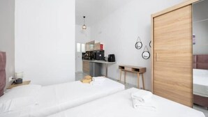 Una habitación de hotel moderna con dos camas, un armario de madera, una pequeña cocina y un reloj fijado a la pared.