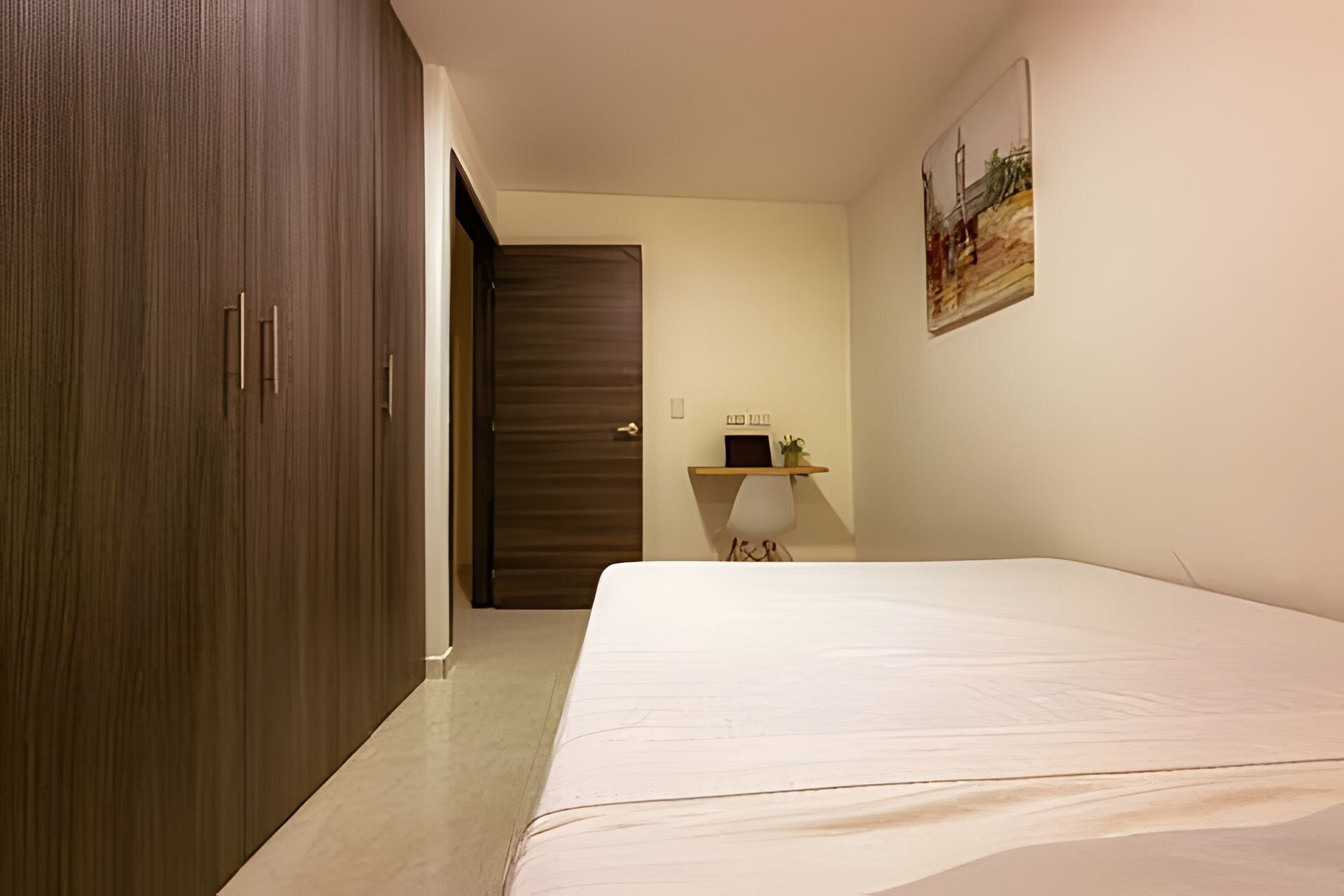 Un dormitorio con una cama, un armario, un escritorio con una planta y un cuadro en la pared.