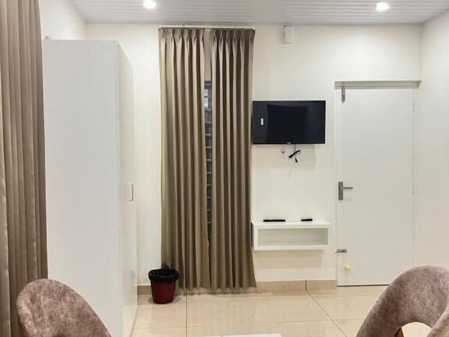 Una sala de estar moderna con dos sillones, una mesa de centro blanca, un televisor montado en la pared y una puerta corredera.