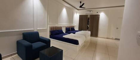 A modern hotel room with a large bed, two blue sofas, a small coffee table, and a ceiling fan.