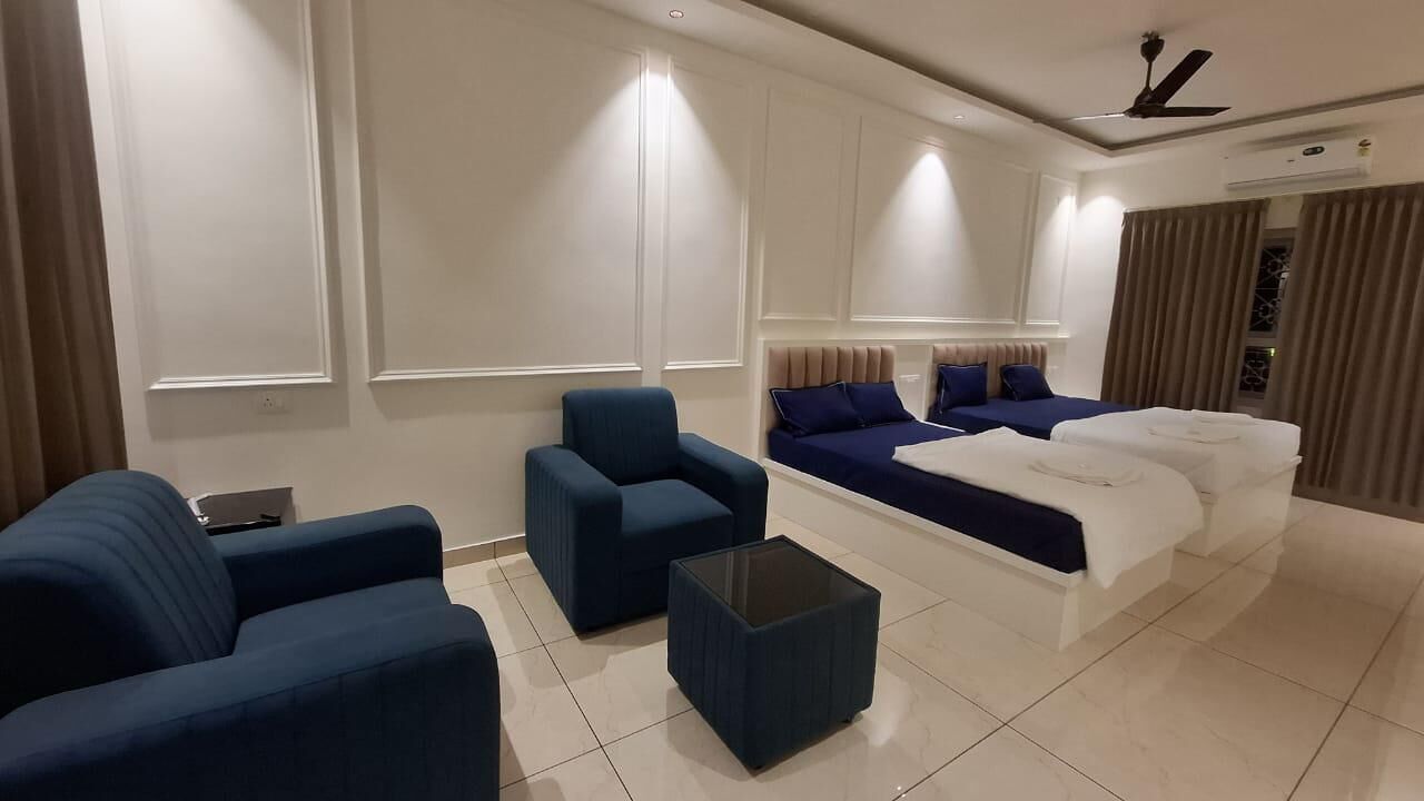 A modern hotel room with a large bed, two armchairs, a coffee table, and a TV.