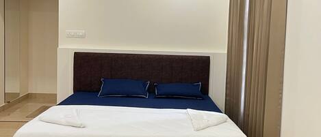 A hotel room with a bed, a bedside table, and a large window with curtains.