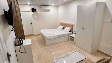 A modern bedroom with a bed, bedside table, wardrobe, and a small dining area with chairs.