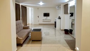 A modern living room with a sofa, a coffee table, a flat-screen TV, and a kitchen area with a microwave and cabinets. - aagneyam grand RESORT (Kozhikode)