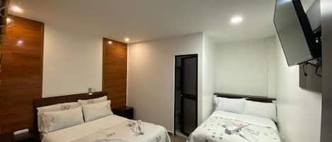 Habitación de hotel con dos camas, un televisor montado en la pared y una puerta que da a otra habitación.