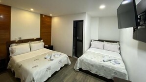 Habitación de hotel con dos camas, un televisor de pantalla plana montado en la pared y una puerta que da a otra habitación.