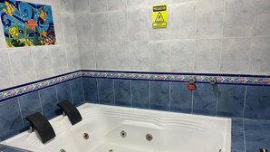 Un baño con una bañera grande, azulejos azules y un letrero de precaución.