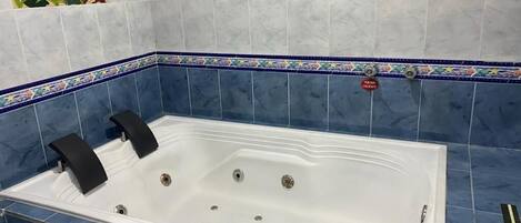 Un baño con una bañera grande, azulejos azules y un letrero de precaución.
