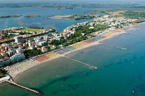 An aerial view of a coastal city with a beach lined with umbrellas and a pier extending into the water. - Chic Retreat for Your Holidays in Grado (Grado)