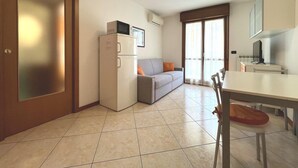 A modern kitchen with a refrigerator, a dining table, and a sofa in a bright room with a large window. - Sweet Holiday Hideaway in Grado for Four Guests (Grado)