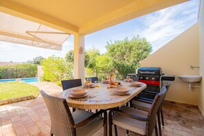 Eine Terrasss mit rundem Esstisch, umgeben von Korbstühlen. Ein Grill ist zur Rechten sichtbar.