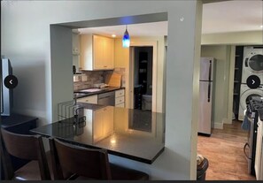 A modern kitchen with a central island, a dining area with chairs, and a washing machine in the background. - Salem Common Cozy Nest (Salem)