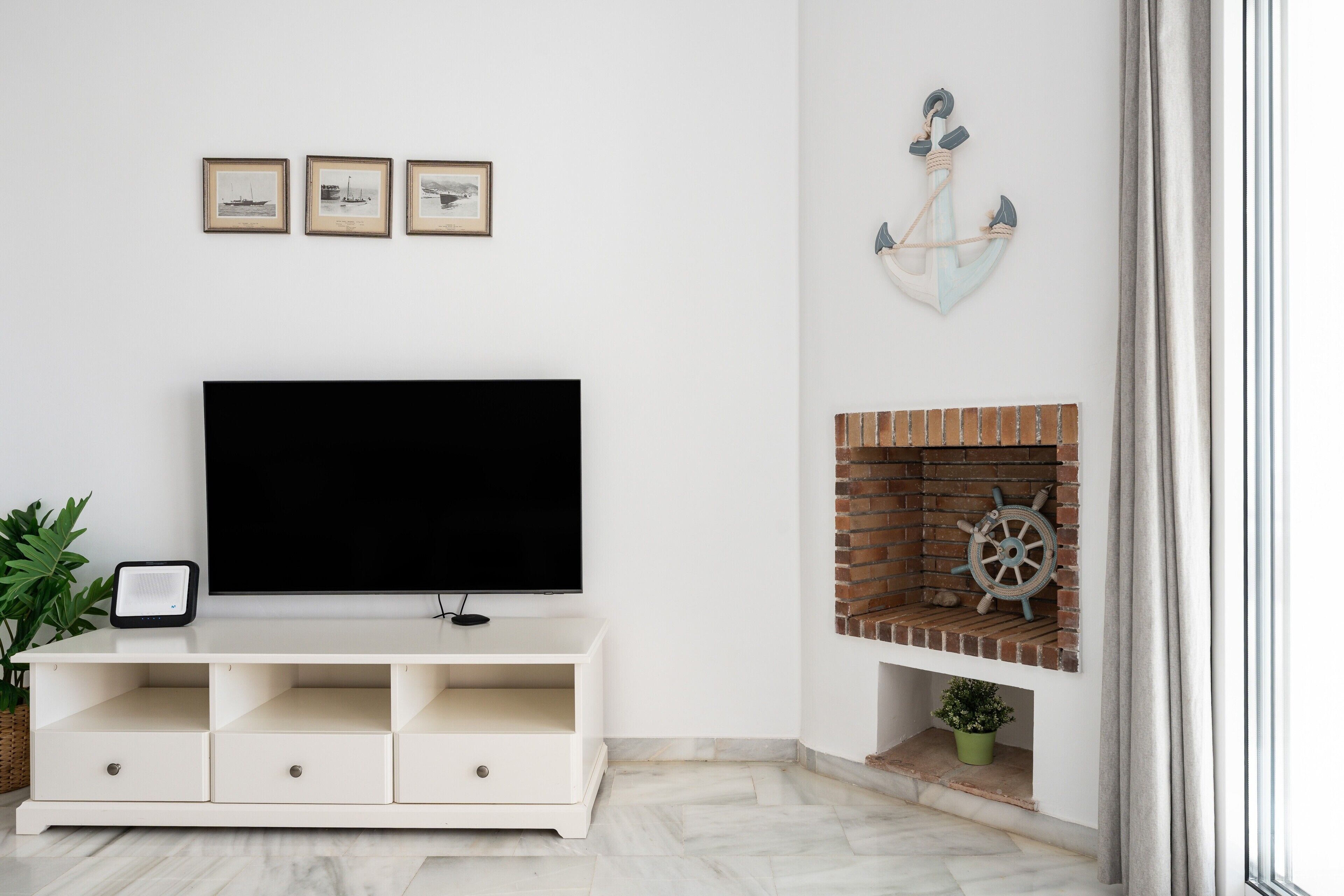A living room with a flat-screen TV, a fireplace with a ship's wheel, and three framed pictures on the wall.