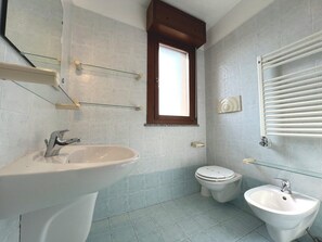 Et badeværelse med vask, toilet, bidet og et vindue.