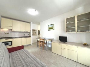 A compact kitchen with a dining area, a TV, and a cabinet with glass doors. - Spacious and Comfortable Holiday Home in Grado (Grado)