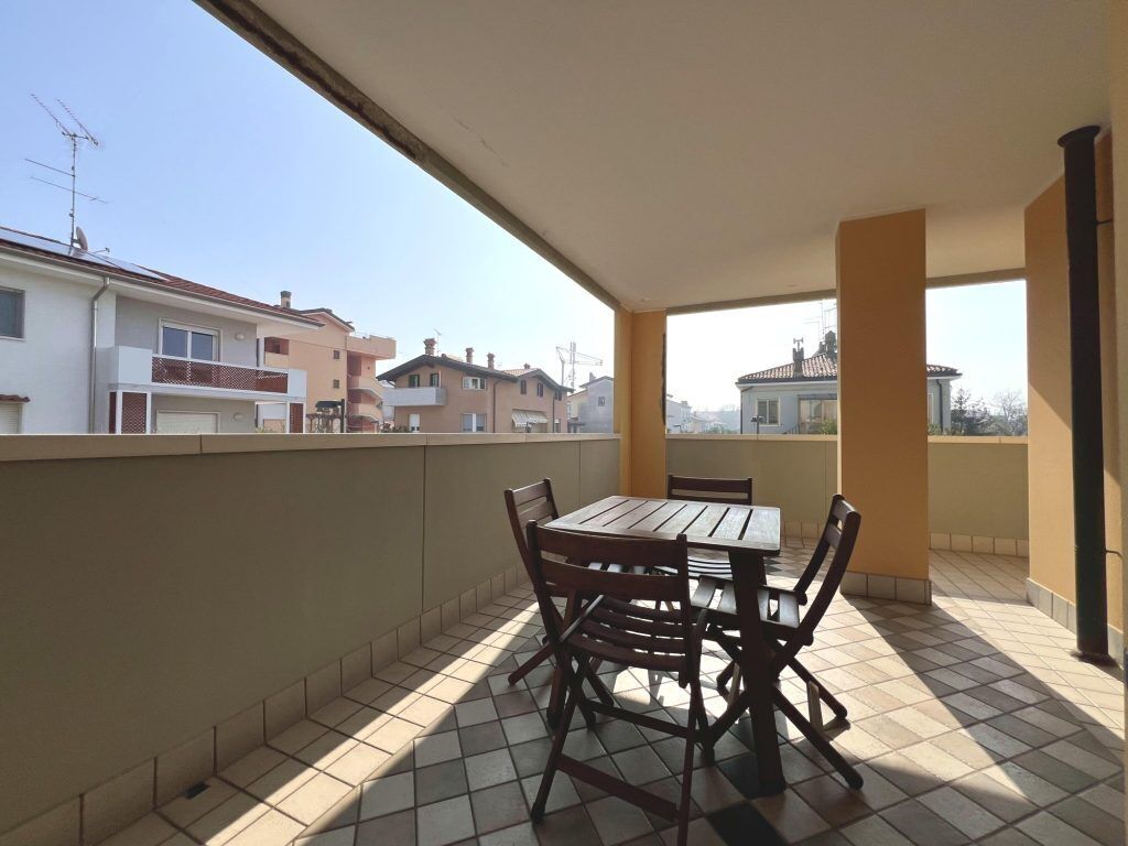 Un balcon avec une table et des chaises, donnant sur un quartier résidentiel avec des maisons.