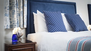 Una cama bien hecha con almohadas blancas y azul marino, una colcha a rayas y un cabecero azul oscuro.