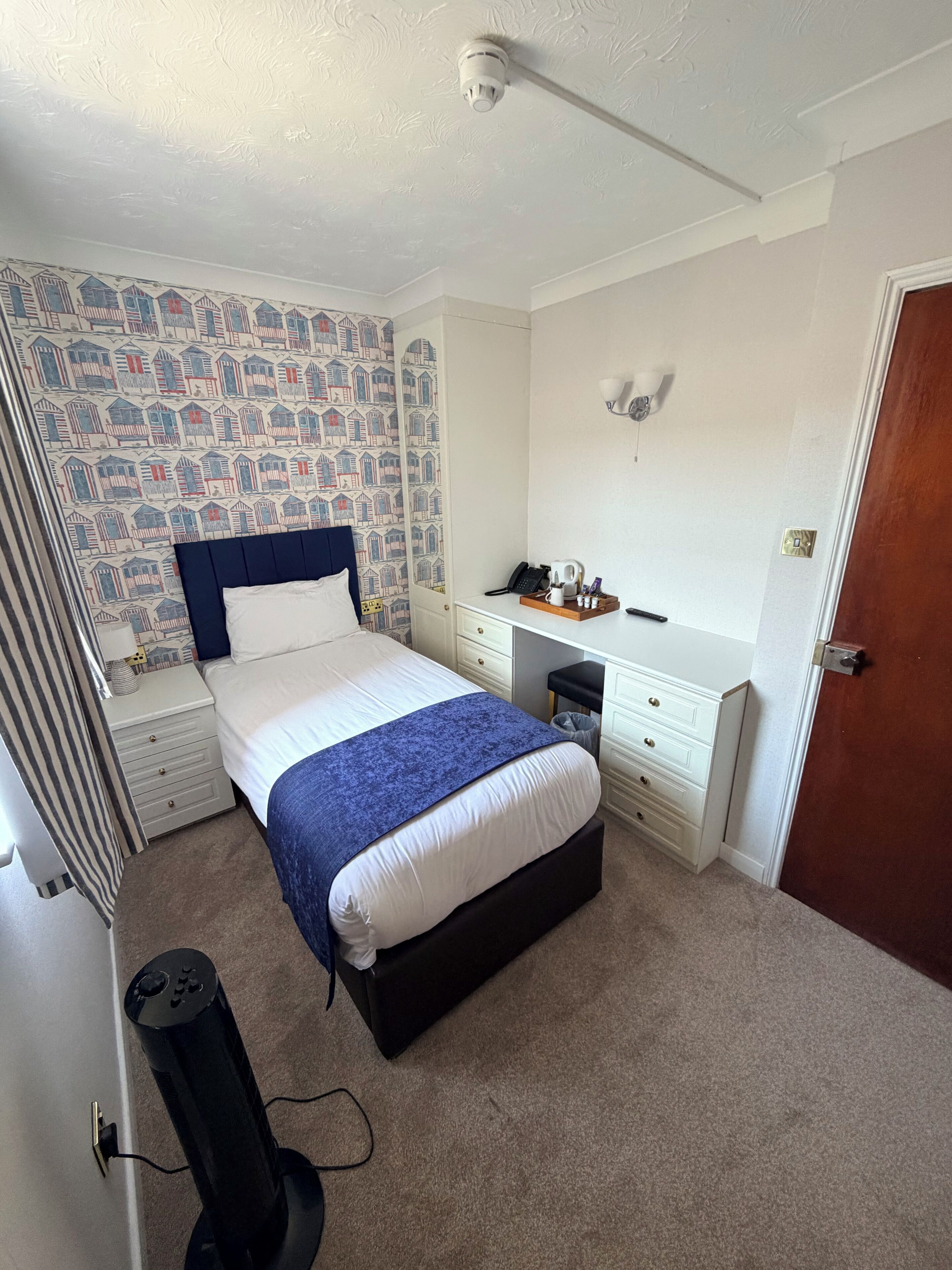 A bedroom with a bed, a desk, a chair, a radiator, and a door.