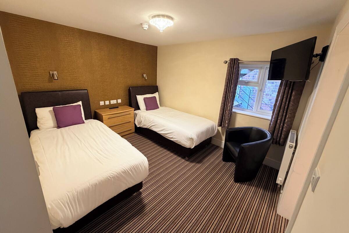 A hotel room with two beds, a TV, a window, and a trash bin.