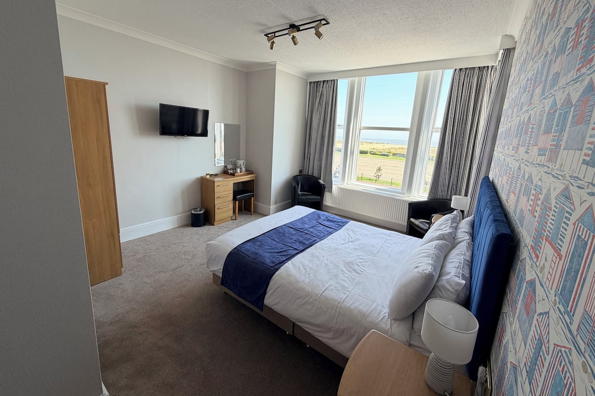 A hotel room with a bed, a desk, a chair, a TV, and a window with a view.