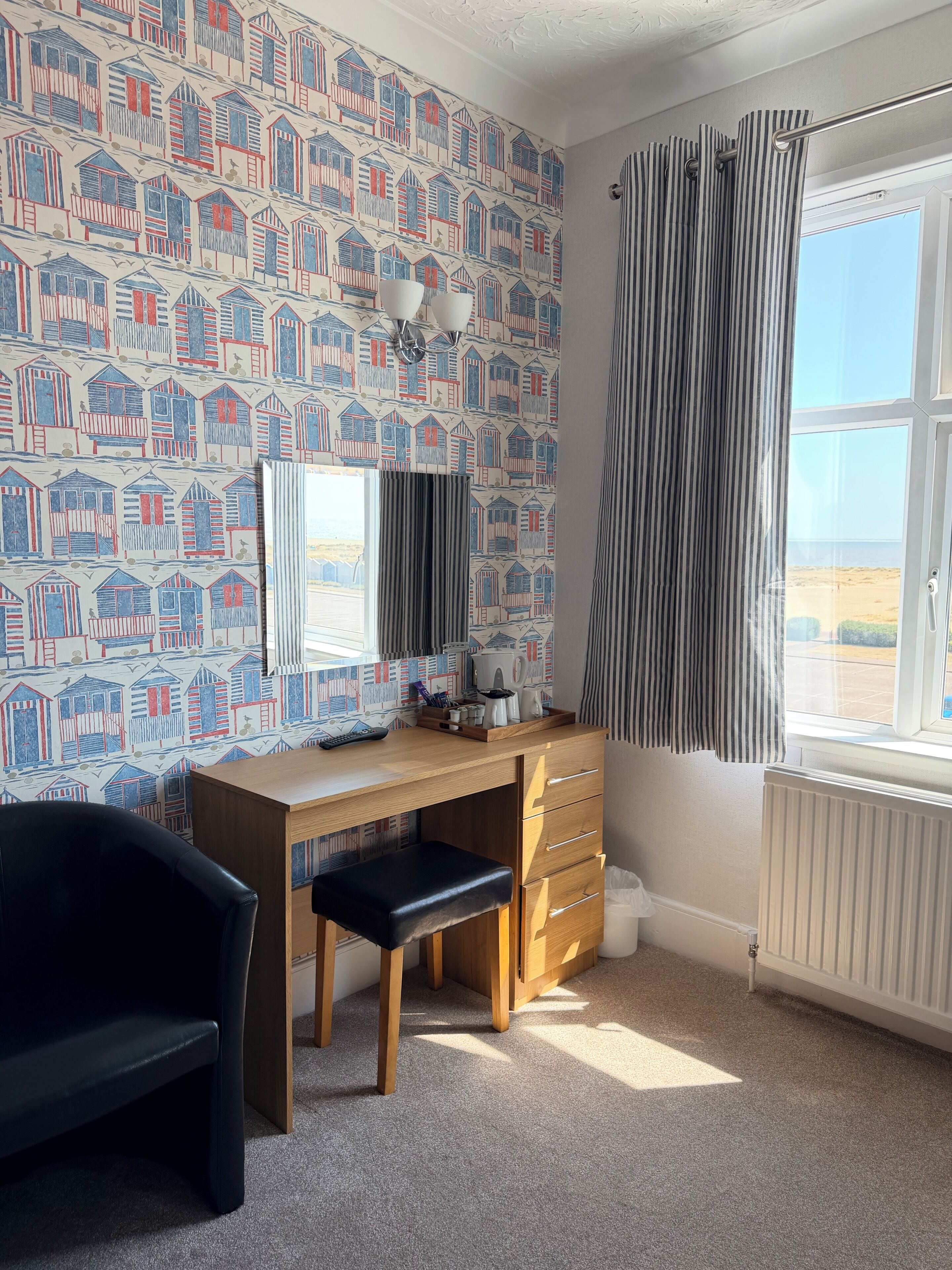 Ein Zimmer mit einem Holztisch, einem schwarzen Stuhl, einer Heizung und einem Fenster mit Vorhängen.
