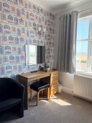Ein Zimmer mit einem Holztisch, einem schwarzen Stuhl, einer Heizung und einem Fenster mit Vorhängen.