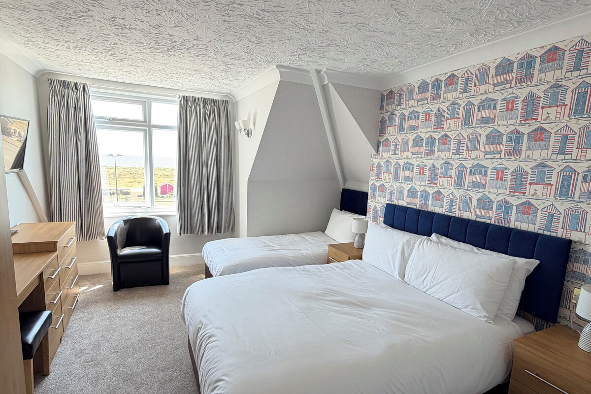 A bedroom with two beds, a desk, a chair, and a patterned wall.