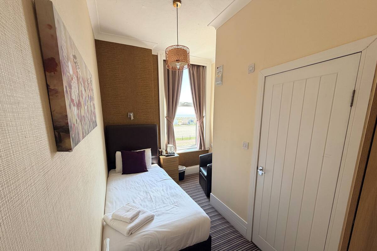 A hotel room with a bed, a desk, a chair, a door, and a window with curtains.
