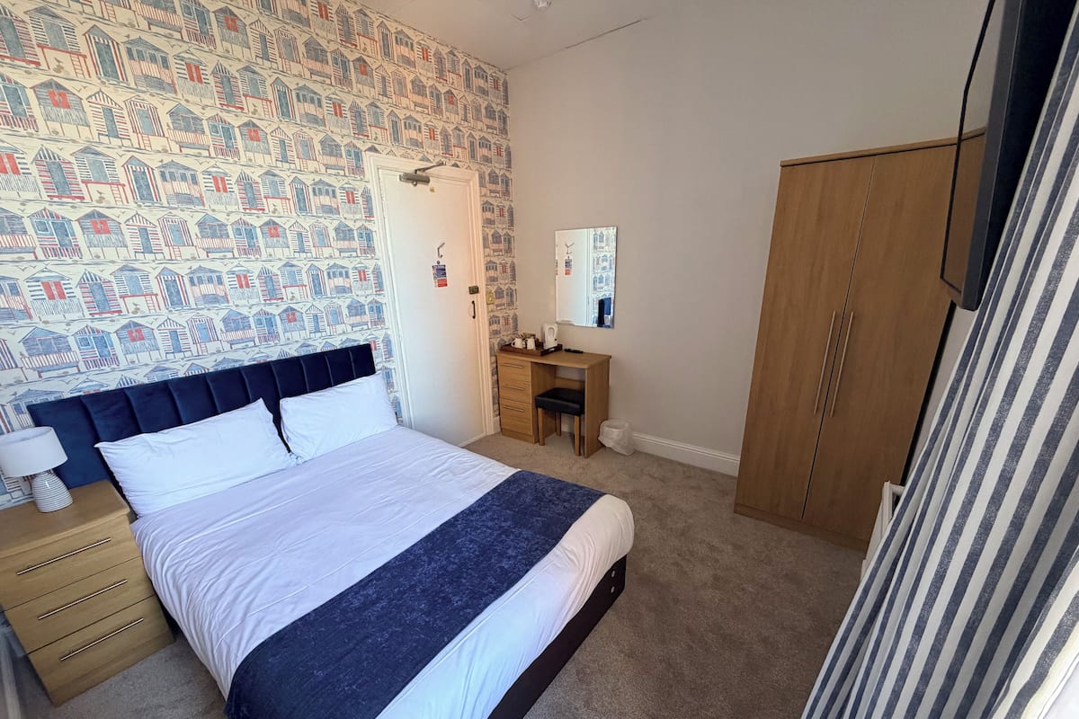Une chambre à coucher avec un lit, un bureau, une armoire et un mur décoré d’un motif.