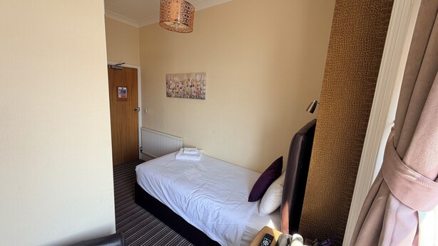 Ein Hotelzimmer mit einem Bett, einem Nachttisch mit Fernbedienung, einem Wasserkocher und einem Telefon.