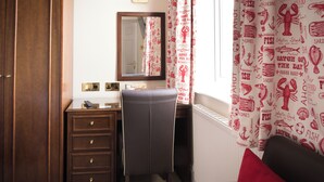 Habitación de hotel con un armario de madera, un escritorio con espejo, una silla y una ventana con cortinas de diseño rojo y blanco.