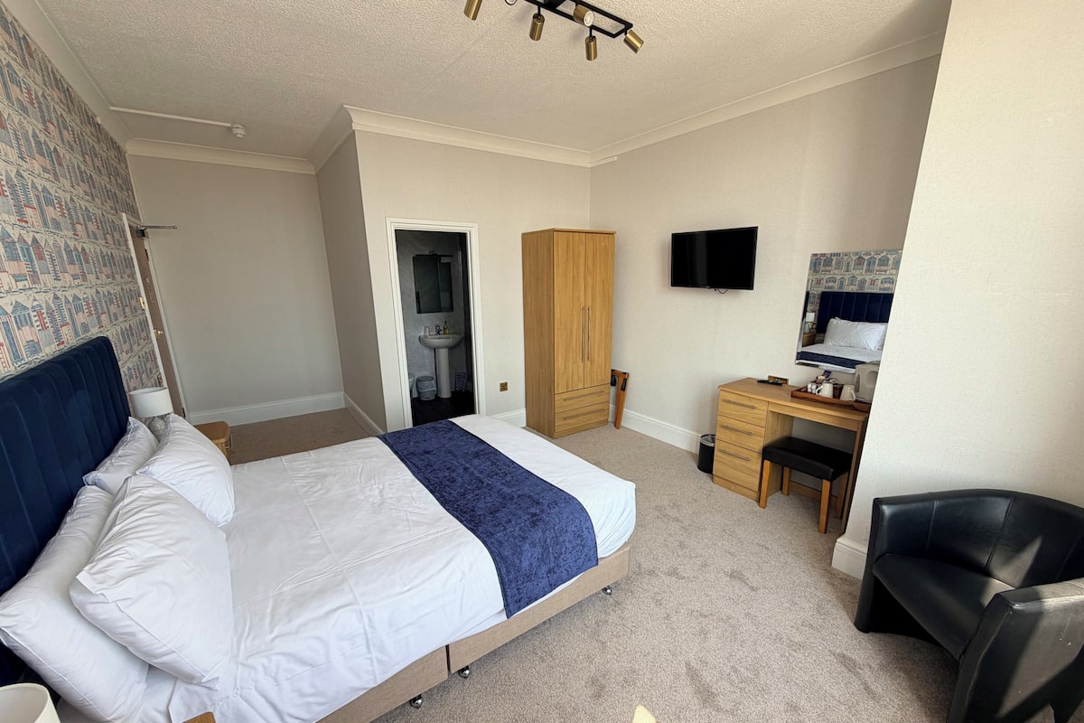 A hotel room with a bed, desk, chair, wardrobe, and a television.