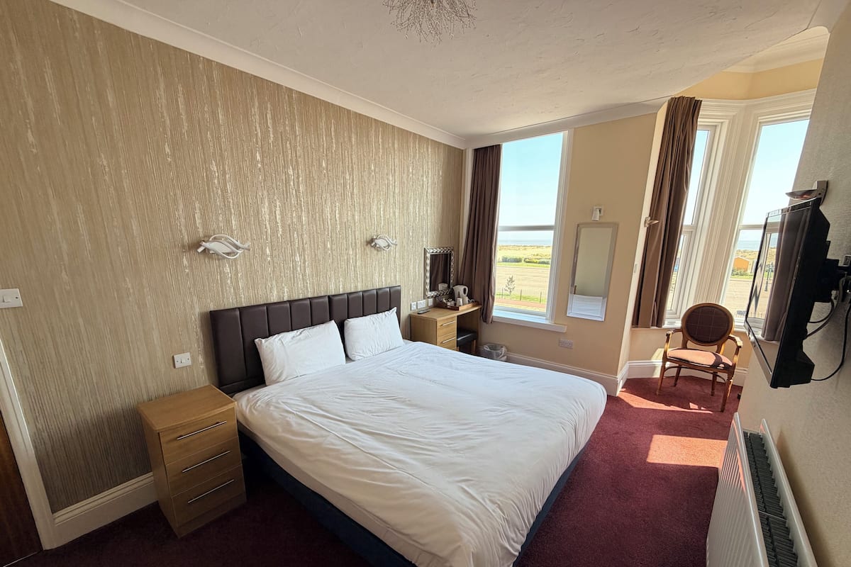 A hotel room with a large bed, bedside tables, a chair, a TV, and a view of the outdoors.