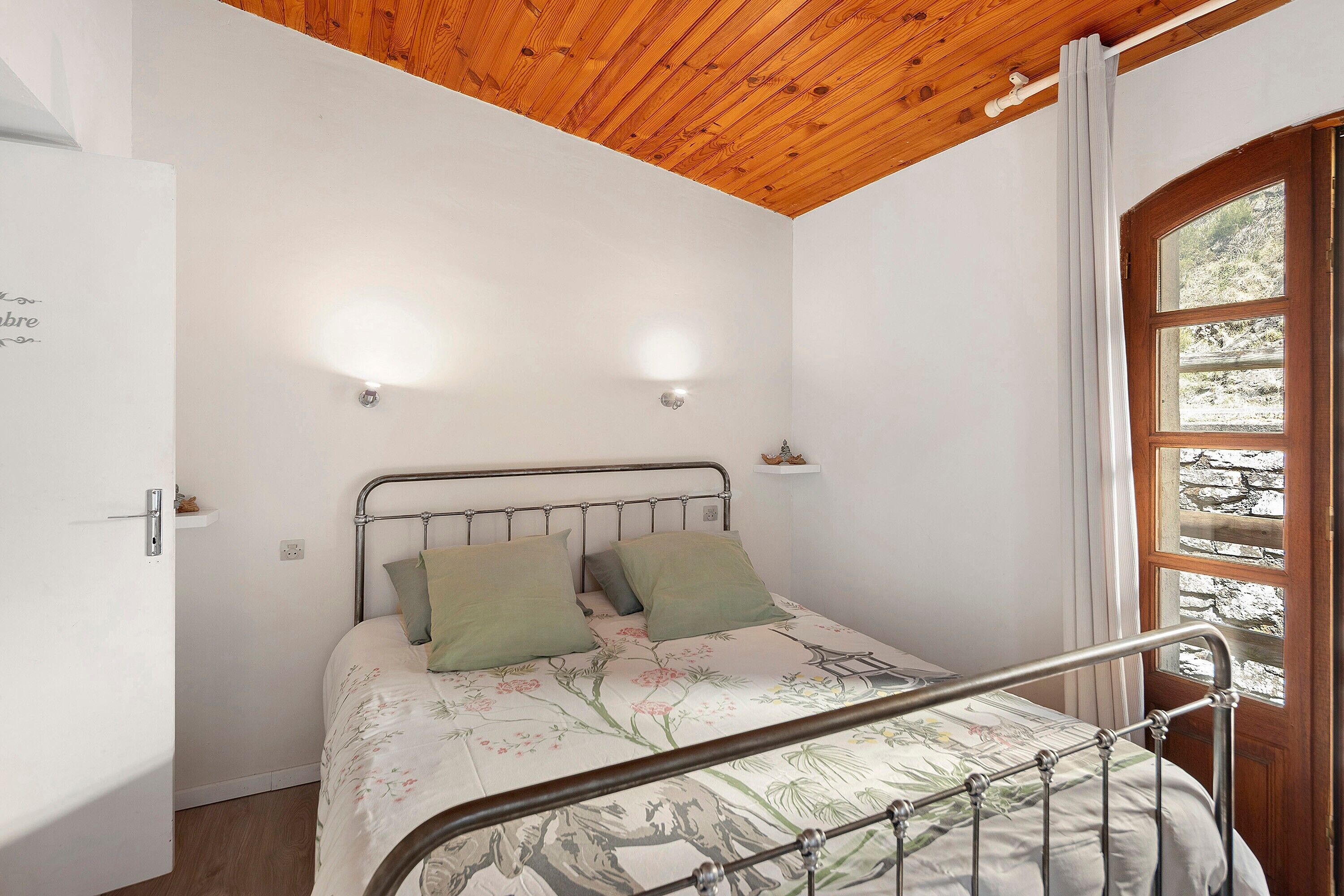 Ein Schlafzimmer mit Holzboden, einem Metallbettgestell und einem Fenster mit Vorhängen.