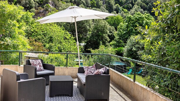 An outdoor patio with wicker furniture, a white umbrella, and a view of a lush green hillside. - Holiday Home 'Maison En Cevennes' with Mountain View, Private Pool and Private Terrace (L'Estréchure)