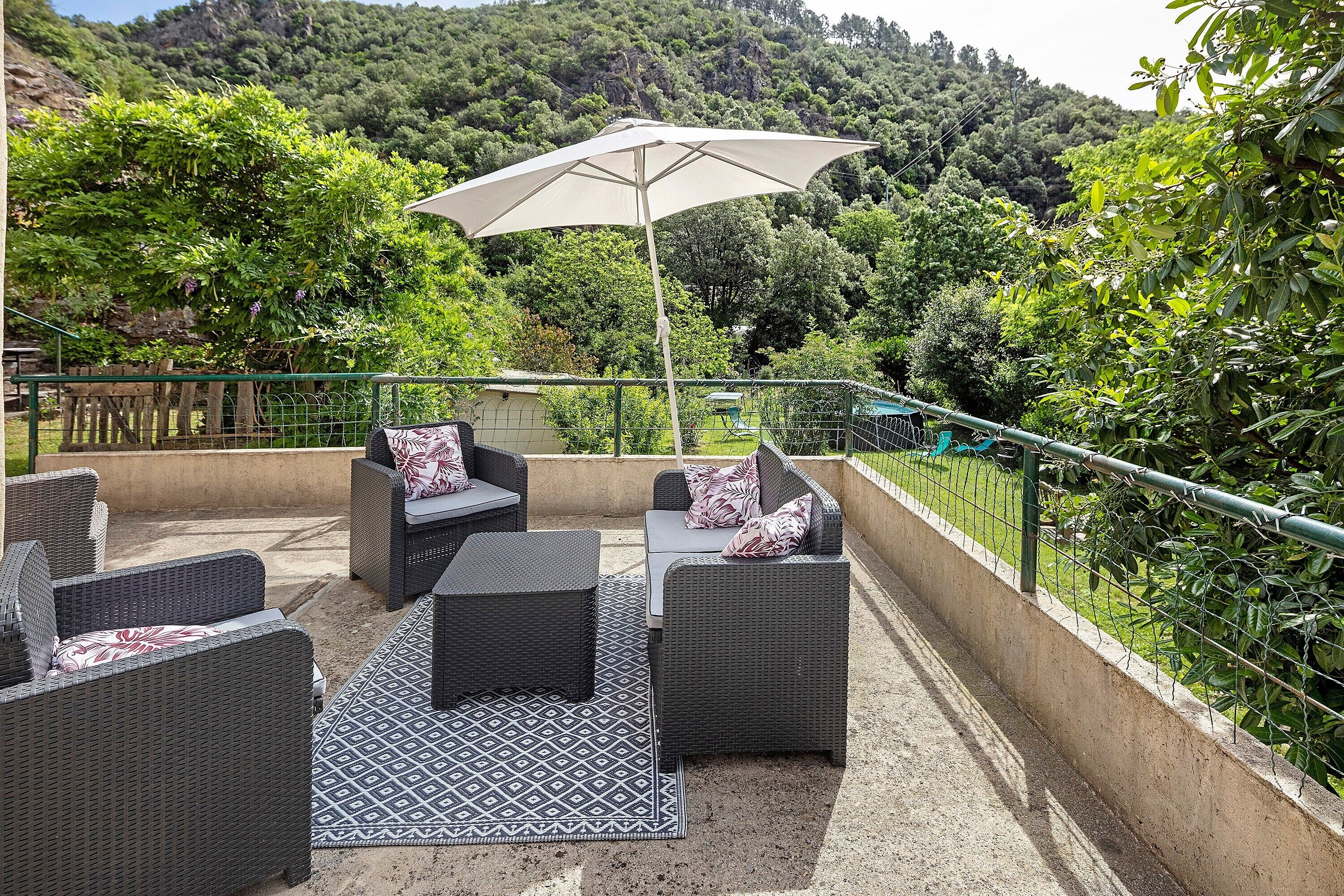 Une terrasse extérieure aménagée avec des meubles en osier, un tapis à motifs et un grand parasol.