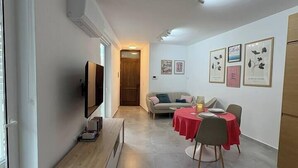 Ett modernt vardagsrum med en tv, en träbänk, en soffa och en matplats med en röd duk.