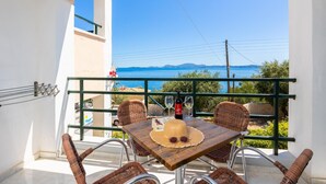 Un balcon avec une table dressée pour deux personnes, agrémenté de chaises en osier, d’un chapeau et d’une bouteille de vin.