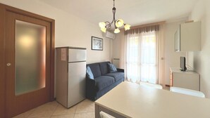 A compact kitchen with a refrigerator, a dining table, and a sofa. - Cozy Holiday Escape Apartment With City View (Grado)