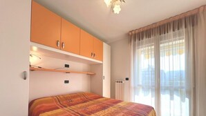 A bedroom with a bed, orange cabinets, a radiator, and a window with curtains. - Cozy Holiday Escape Apartment With City View (Grado)