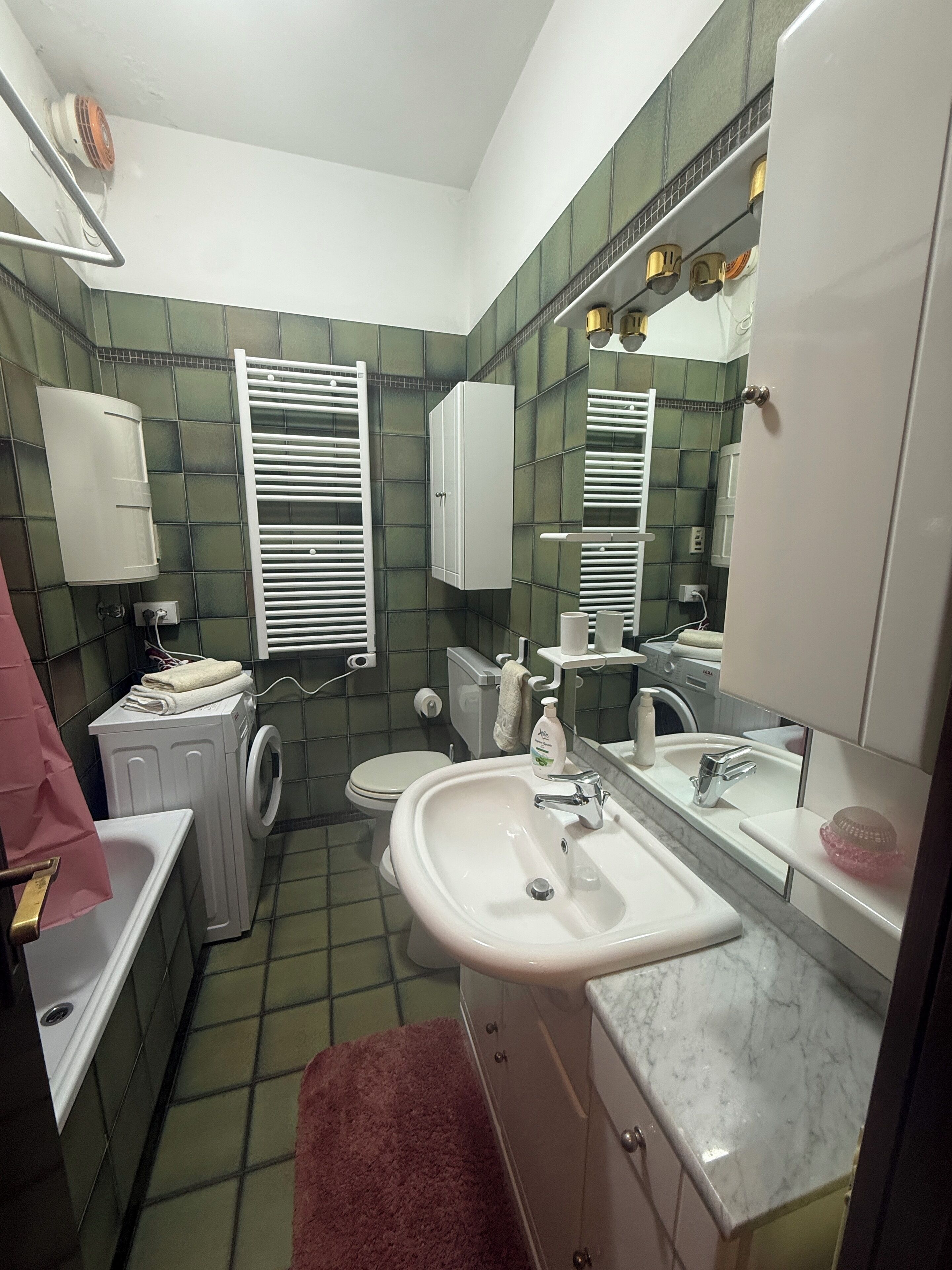 A compact bathroom with a white sink, a toilet, a washing machine, and a mirror.
