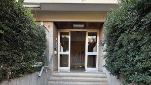 A building entrance with stone steps leading up to a glass door, surrounded by greenery. - Fronte mare con terrazza e garage (Marina di Andora)
