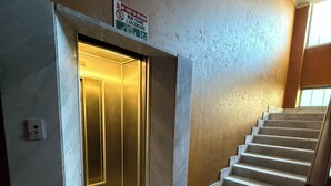 A modern interior with a marble staircase, a lit elevator, and a sign indicating a fire safety protocol. - Fronte mare con terrazza e garage (Marina di Andora)